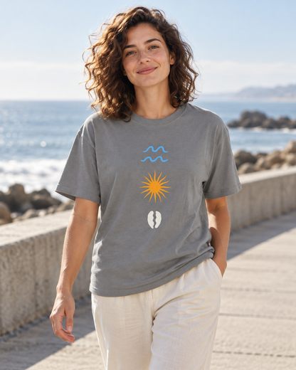 AI lifestyle mockup: grey Daybreak T-shirt worn from the front, showing blue waves, a golden sun and an ivory seed motif.